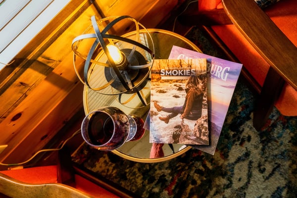 Side table with a glass of red wine and Smoky Mountains and Gatlinburg vacation guides in a PlumCove cabin